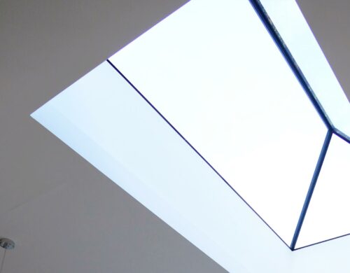 View of a large rectangular skylight with a minimal frame, letting in bright natural light against a white ceiling.