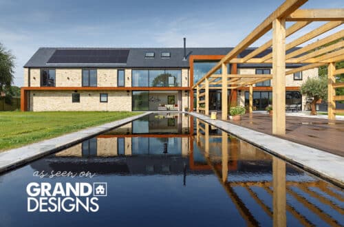 Modern, two-story house with solar panels, large windows, and a reflecting pool.