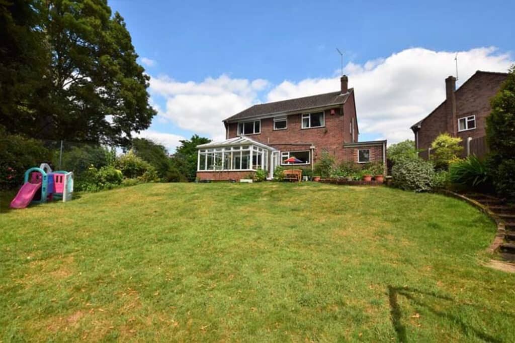 Two-story brick house with a sunroom and a large grassy backyard. A children's slide is on the left, and there are steps leading down from the right side.