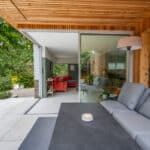 Thumbnail of http://Modern%20outdoor%20patio%20with%20a%20gray%20couch%20and%20table,%20leading%20through%20sliding%20glass%20doors%20to%20an%20indoor%20living%20area%20with%20a%20red%20sofa.%20Greenery%20visible%20outside.