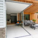 Thumbnail of http://Modern%20patio%20with%20open%20sliding%20glass%20doors%20revealing%20indoor%20and%20outdoor%20seating%20areas.%20Features%20a%20sofa,%20table,%20and%20plants%20on%20a%20tiled%20floor.%20Walls%20include%20wooden%20paneling%20and%20white%20siding.