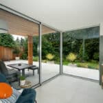 Thumbnail of http://Modern%20interior%20with%20a%20large%20glass%20door%20opening%20to%20a%20patio%20and%20garden.%20A%20blue%20armchair%20with%20an%20orange%20cushion%20is%20in%20the%20foreground,%20and%20a%20lamp%20and%20side%20table%20are%20nearby.