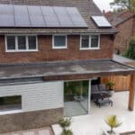 Thumbnail of http://A%20modern%20two-story%20house%20with%20solar%20panels%20on%20the%20roof%20and%20a%20flat-roof%20extension%20featuring%20large%20windows.%20The%20backyard%20has%20a%20paved%20patio%20area%20with%20outdoor%20furniture.