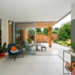 Thumbnail of http://Modern%20indoor%20space%20with%20large%20glass%20doors%20opening%20to%20a%20patio.%20Features%20a%20chair,%20potted%20plant,%20and%20a%20view%20of%20a%20garden%20with%20trees%20and%20a%20wooden%20fence.