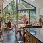 Thumbnail of http://Stylish%20kitchen%20with%20large%20windows%20and%20skylights,%20modern%20wooden%20furniture,%20and%20a%20view%20of%20a%20lush%20garden%20with%20outdoor%20seating%20and%20steps%20leading%20to%20a%20house.