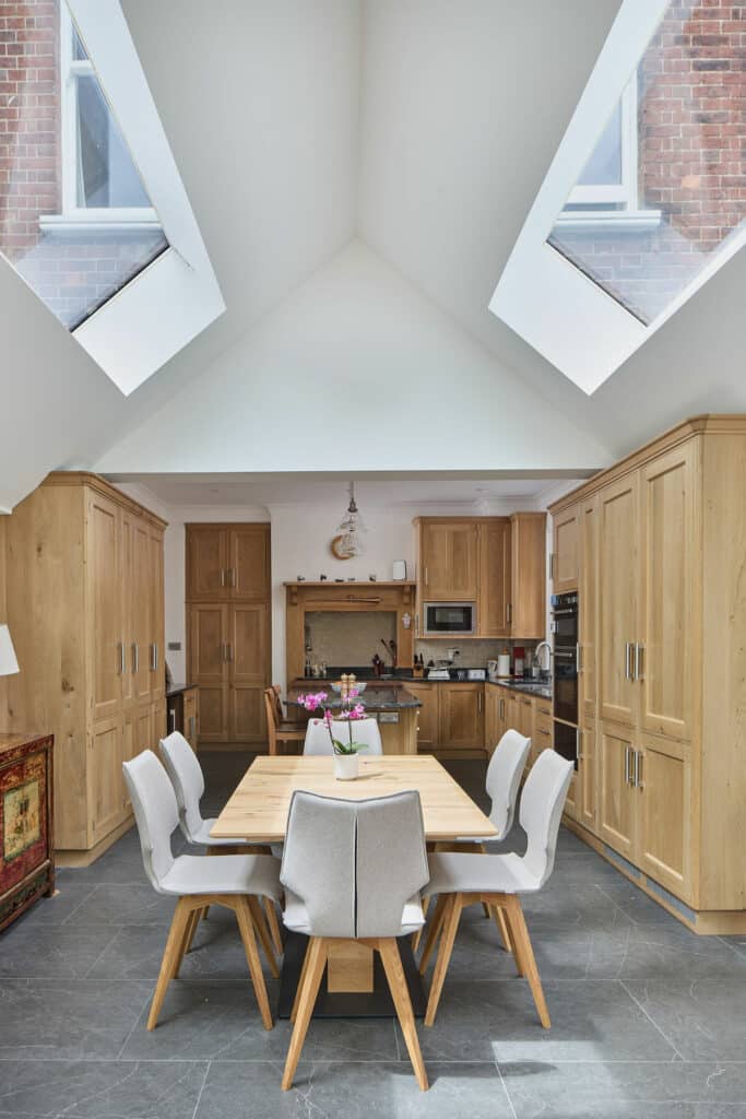 Spacious kitchen with high ceiling and skylights, featuring wooden cabinets, a dining table with six chairs, and modern appliances.