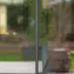 Thumbnail of http://A%20close-up%20view%20of%20a%20clean%20glass%20window%20with%20a%20vertical%20black%20metal%20frame,%20showing%20a%20blurred%20outdoor%20scene%20with%20greenery%20and%20a%20drive%20in%20the%20background.