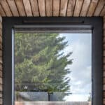 Thumbnail of http://A%20rectangular%20window%20with%20a%20black%20frame%20is%20set%20in%20a%20brick%20wall,%20reflecting%20a%20large%20evergreen%20tree%20and%20a%20cloudy%20sky%20outside.