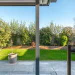 Thumbnail of http://View%20from%20an%20open%20sliding%20glass%20door%20looking%20out%20onto%20a%20patio,%20green%20lawn,%20potted%20plant,%20and%20bushes%20along%20a%20fence%20under%20a%20clear%20blue%20sky.