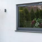 Thumbnail of http://A%20modern%20grey-framed%20window%20on%20a%20white%20wall%20reflects%20green%20trees%20and%20contains%20a%20vase%20with%20mixed%20flowers%20inside.