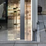 Thumbnail of http://A%20modern%20dining%20area%20with%20upholstered%20chairs%20and%20a%20spotty%20tablecloth%20is%20seen%20through%20glass%20doors,%20with%20a%20side%20table%20and%20brick%20feature%20wall%20inside,%20and%20a%20paved%20patio%20outside.