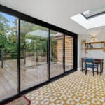Thumbnail of http://Room%20with%20yellow%20patterned%20tiled%20floor,%20glass%20sliding%20doors%20opening%20to%20a%20wooden%20decking,%20and%20a%20skylight%20above%20a%20small%20desk%20with%20a%20chair;%20green%20trees%20visible%20outside.