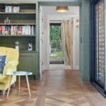 Thumbnail of http://A%20living%20room%20with%20a%20yellow%20sofa,%20built-in%20green%20bookcase,%20parquet%20wooden%20floor,%20and%20large%20glass%20door%20leading%20to%20a%20hallway%20with%20a%20view%20outside.