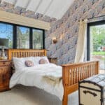 Thumbnail of http://A%20bedroom%20with%20floral%20wallpaper,%20a%20wooden%20bed,%20white%20bed%20linen,%20two%20bedside%20tables,%20a%20vintage%20trunk%20at%20the%20foot%20of%20the%20bed,%20and%20glass%20doors%20opening%20to%20a%20garden.