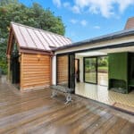 Thumbnail of http://A%20modern%20house%20with%20a%20wooden%20exterior,%20large%20sliding%20glass%20doors,%20and%20a%20deck%20area%20overlooking%20a%20garden%20with%20trees.