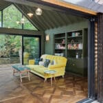 Thumbnail of http://A%20modern%20living%20room%20with%20a%20yellow%20sofa,%20built-in%20bookshelves,%20and%20glass%20sliding%20doors%20opens%20to%20a%20balcony%20overlooking%20trees.%20Parquet%20wood%20flooring%20and%20pendant%20lights%20are%20visible.