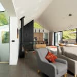 Thumbnail of http://Modern%20open-plan%20living%20area%20with%20grey%20furniture,%20a%20wood-burning%20stove,%20large%20windows,%20glass%20staircase,%20and%20natural%20light%20overlooking%20green%20hills.