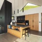 Thumbnail of http://Modern%20kitchen%20with%20light%20wood%20cupboards,%20black%20worktops,%20an%20island%20with%20stools,%20pendant%20lights,%20and%20high%20ceilings.%20Sunlight%20streams%20in%20through%20geometric%20windows.