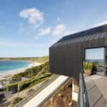 Thumbnail of http://Modern%20house%20with%20large%20glass%20doors%20and%20solar%20panels%20overlooks%20a%20sandy%20beach%20and%20sea%20under%20a%20partly%20cloudy%20sky.%20Outdoor%20terrace%20and%20coastal%20landscape%20are%20visible.