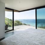 Thumbnail of http://A%20modern%20bedroom%20with%20large%20floor-to-ceiling%20windows%20and%20a%20sliding%20door%20opening%20to%20a%20patio,%20offering%20a%20clear%20view%20of%20the%20sea%20and%20coastline.