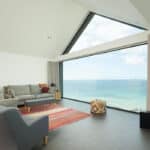 Thumbnail of http://Modern%20living%20room%20with%20grey%20sofas,%20a%20red%20rug,%20and%20a%20large%20window%20offering%20a%20clear%20view%20of%20the%20sea%20and%20sky.%20A%20flat-screen%20TV%20is%20mounted%20on%20the%20right%20wall.