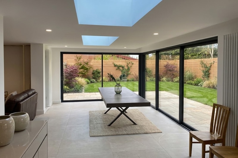 Modern extension with black framed bifold doors opening onto garden, featuring skylight and dining table.