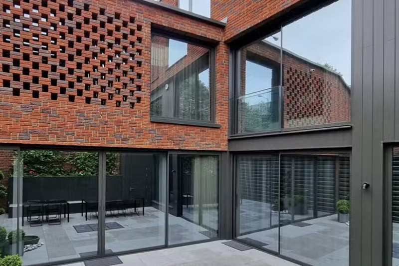 Red brick courtyard with Sunflex bifold doors and sliding glass doors opening onto paved terrace area.