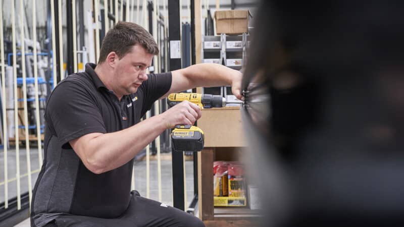Technician assembling bifold door components at Sunflex UK factory using DeWalt drill.