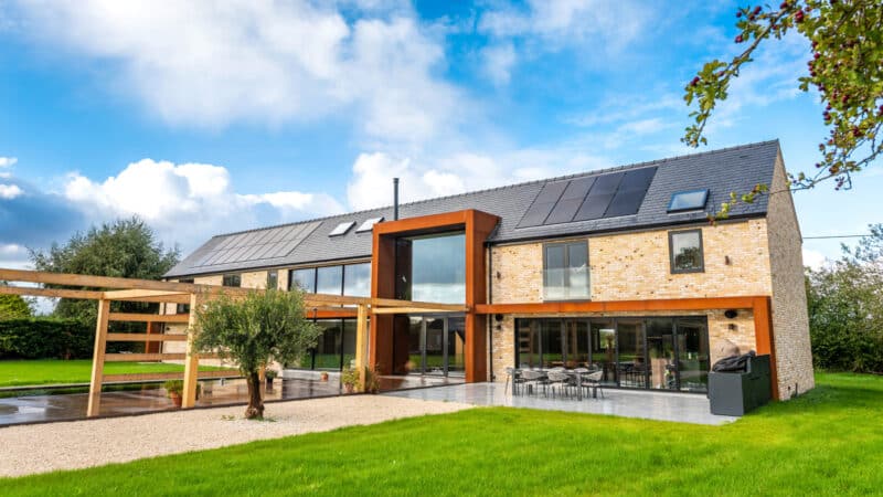 Modern brick house with orange-framed bifold doors and sliding glass systems opening onto paved terrace and lawn.