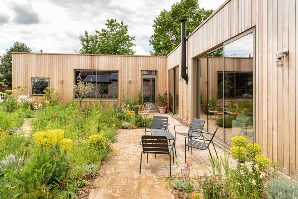 Modern timber-clad Suffolk eco-home with large bifold doors opening onto paved courtyard garden with seating.