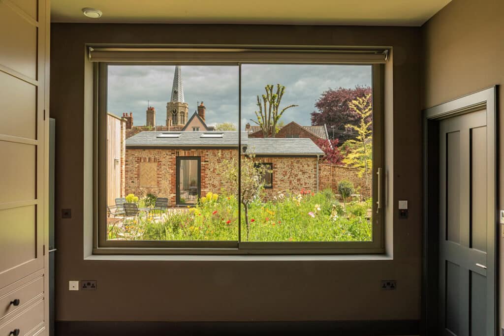 Large sliding doors with garden view from contemporary Suffolk eco-home interior, showing manicured garden and period architecture beyond.