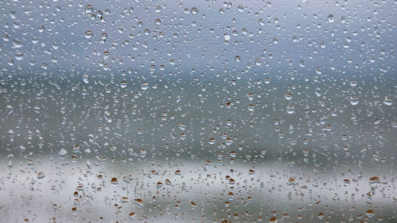 SF80 high performance sliding door viewed from inside during heavy rain, demonstrating weather resistance with water droplets covering glazed panel.