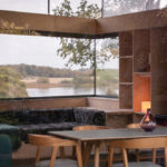 Thumbnail of http://Interior%20view%20of%20Rescobie%20Pavilion%20with%20floor-to-ceiling%20glazing%20framing%20river%20landscape,%20wooden%20dining%20table,%20built-in%20seating,%20and%20shelving.
