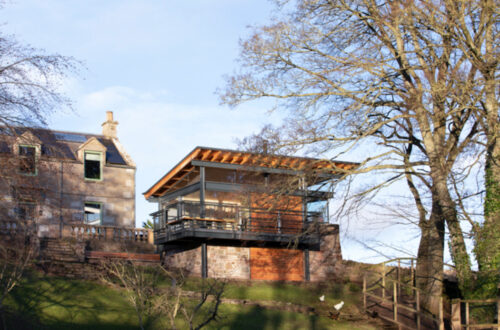 Modern glass pavilion extension with wooden cladding and bifold doors attached to historic Scottish stone building.